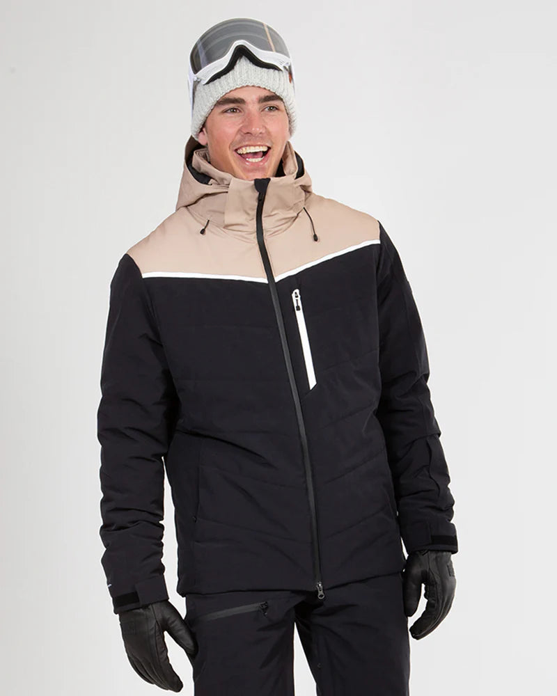 Smilende mand i sort skijakke med beige skuldre, hvid hue og skibriller på hovedet